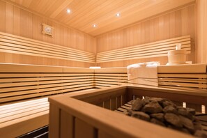 A wooden sauna with benches and a stone basin. - Portis Appartements (Dienten am Hochkoenig)