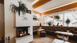 A cozy room with a fireplace, wooden ceiling beams, a bench seating area, and various potted plants.