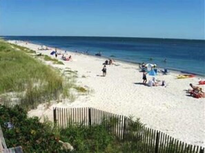 A beach with a wooden fence, people relaxing, and beachgoers in the distance. - Outstanding Rental Home In Gated Great Island Ocean Club (2338) (Yarmouth)