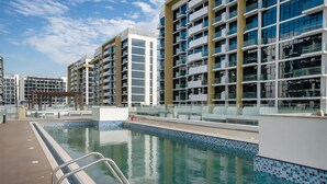 Une piscine dont le bord est revêtu de carrelage, entourée de bâtiments modernes dotés de balcons.