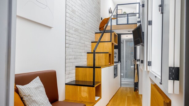 A compact living space with a wooden staircase, a sofa, and a small kitchen area. - Saudade Micro Lofts (Lisbon)