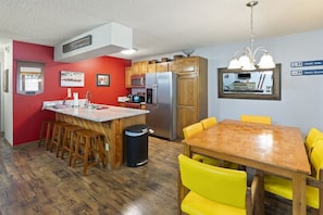 A compact kitchen with a central island, wooden cabinets, and a dining area with yellow chairs.