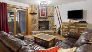 A cozy living room with leather sofas, a stone fireplace, a television, and a ski rack. - Phoenix 207 2 Bedroom Condo by RedAwning (Steamboat Springs)