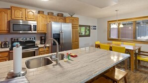 A kitchen with wooden cabinets, stainless steel appliances, a marble countertop, and a dining area with yellow chairs. - Phoenix 207 2 Bedroom Condo by RedAwning (Steamboat Springs)