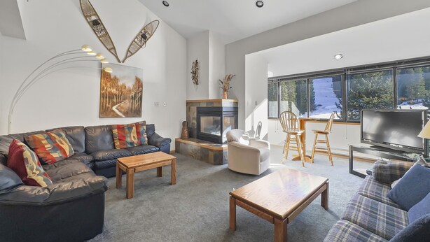 Un salon moderne doté d’une cheminée, d’un canapé en cuir, d’une table basse en bois et d’une grande fenêtre offrant une vue sur les arbres et la neige.