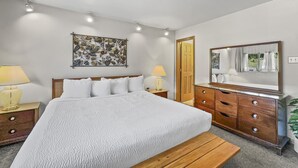 Une chambre à coucher comprenant un lit, des tables de chevet, une commode, un miroir et une œuvre d’art aux motifs floraux accrochée au mur.