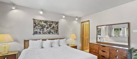 Un dormitorio con cama, mesitas de noche, cómoda, espejo y una obra de arte floral en la pared.
