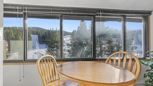 Un coin repas avec une table ronde en bois et deux chaises, de grandes fenêtres offrant une vue sur un paysage enneigé et des arbres.