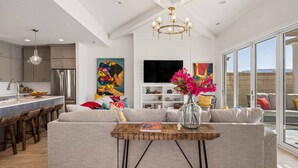 A modern kitchen with a central island, a dining area with a sofa and a coffee table, and a living room with a TV and artwork.