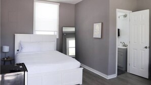 A bedroom with a bed, a bedside table, a mirror, a door, and a window.