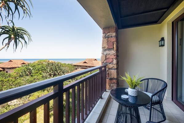 A balcony with a view of the sea, a potted plant, and a dining table with chairs. - Zimbali Coastal Resort - Luxurious Apartments (Ballito)