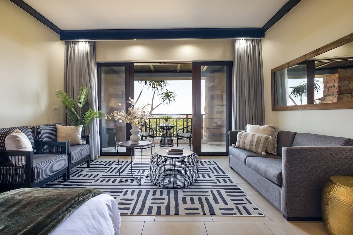 A modern living room with a sofa, a coffee table, and a balcony with a view.