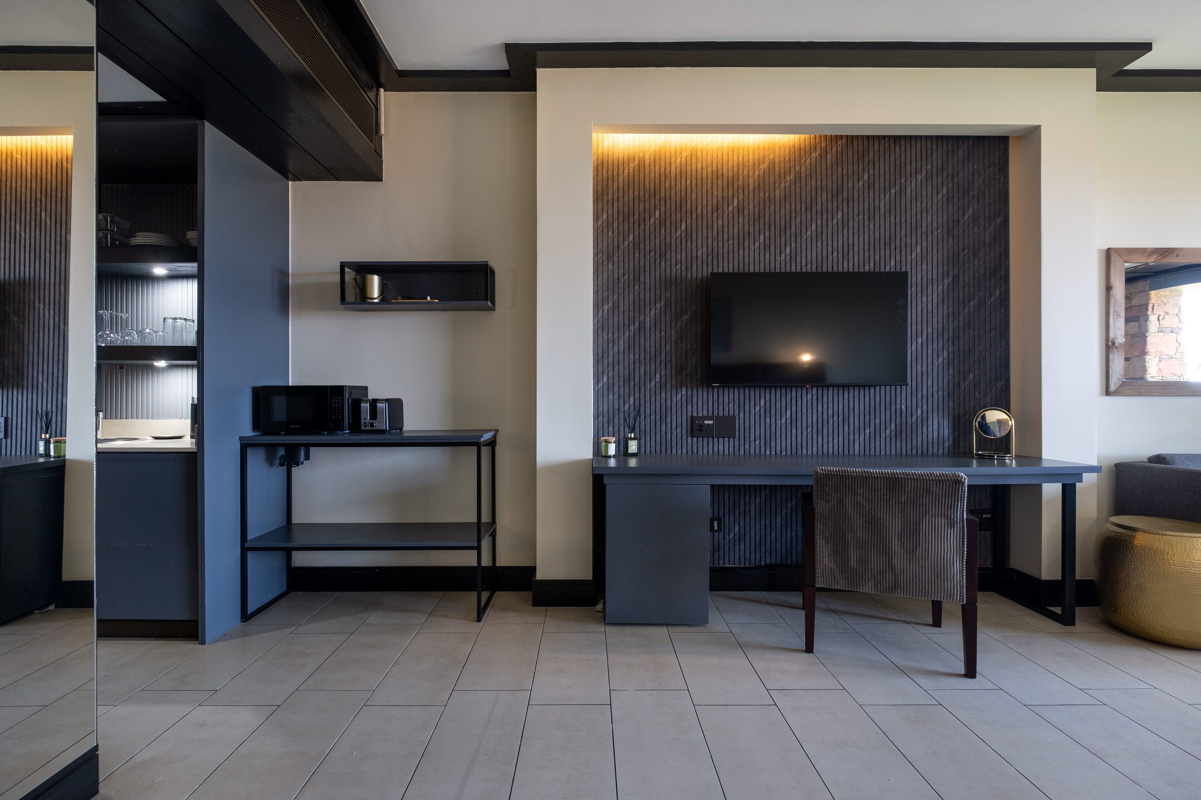 A modern kitchen with a built-in microwave, a small dining area with a table and chair, and a flat-screen TV mounted on a textured wall.