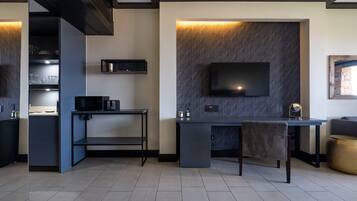 A modern kitchen with a built-in microwave, a small dining area with a table and chair, and a flat-screen TV mounted on a textured wall.