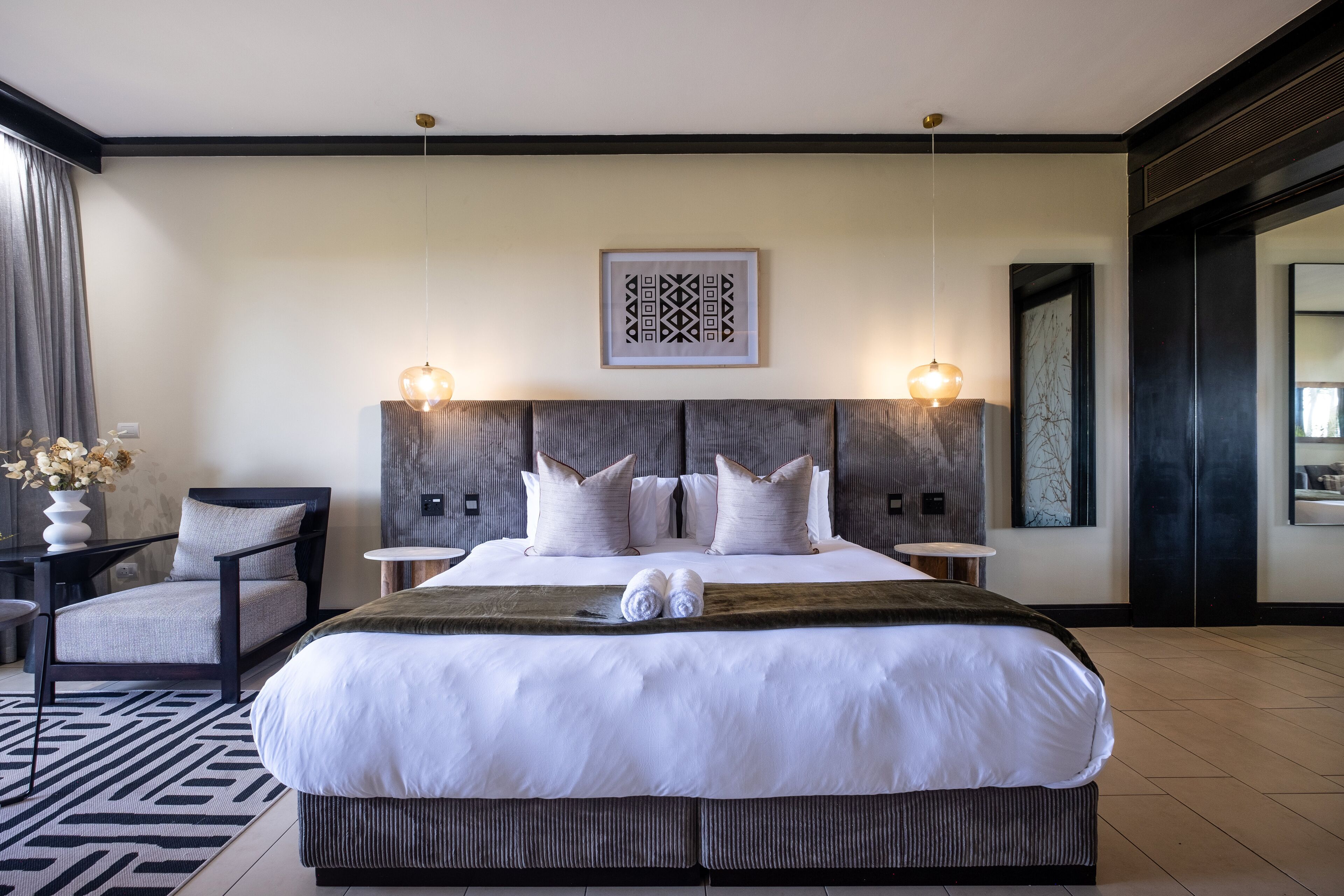 A modern hotel room with a large bed, two bedside tables, a chair, and a large mirror.