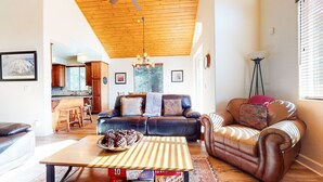 A living room with a wooden ceiling, a sofa, a coffee table with a tray of snacks, and a view into the kitchen. - Beautiful Custom Home. Private Hot Tub, Gas Grill, Short Walk to The Village (Mammoth Lakes)