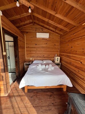 A wooden cabin room with a bed, two bedside tables, a heater, and a door leading outside. - family motel bungalov (Kesan)
