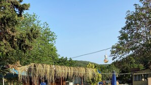An outdoor dining area with wooden tables and chairs, a pool, and a thatched-roof structure. - family motel bungalov (Kesan)