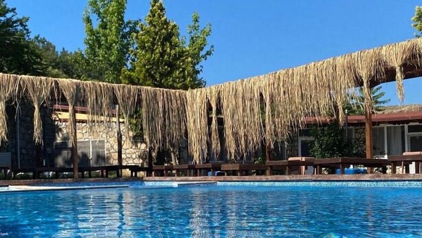 A clear blue pool with a thatched roof structure in the background. - family motel bungalov (Kesan)
