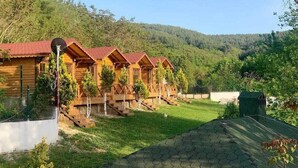 A row of wooden cabins with red roofs, surrounded by a lush green landscape and hills in the background. - family motel bungalov (Kesan)