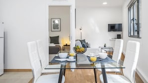 A modern dining area with a glass table, white chairs, and a bowl of fruit. - Funchal Central Loft by Homie (Funchal)
