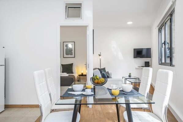 Un comedor moderno con una mesa de vidrio, sillas blancas y un cuenco de fruta.