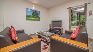 A living room with a sofa set, a coffee table, a flat-screen TV, and a painting on the wall. - Xplore Indo - Onella (Kotagiri)