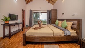 A bedroom with a wooden bed, a television on a side table, and a window with curtains. - Xplore Indo - Onella (Kotagiri)
