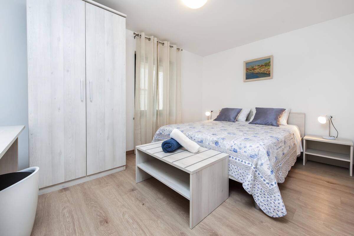 A bedroom with a bed, a bedside table, a nightstand, a wardrobe, and a window with curtains.