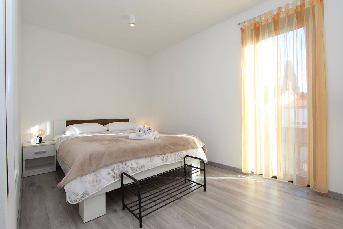 A bedroom with a bed, bedside table, lamp, and a window with curtains.