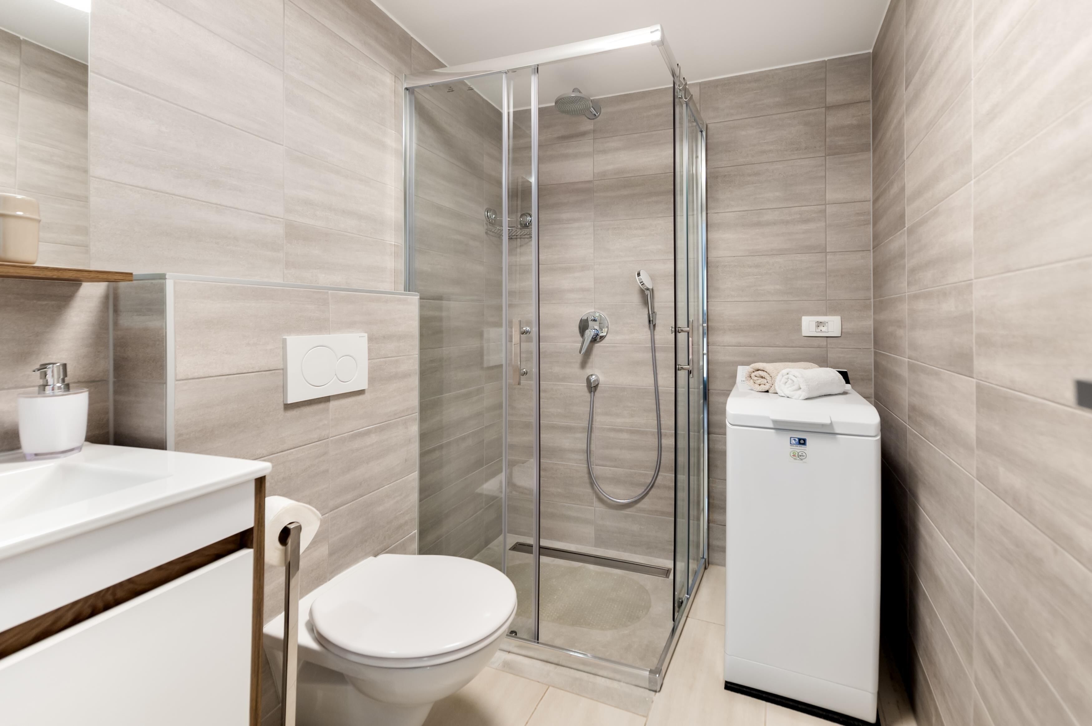 Ein modernes Badezimmer mit einer Duschkabine, einer Toilette und einer integrierten Waschmaschine.