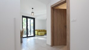 A modern interior with a wooden door, a yellow sofa, and a large glass door leading to an outdoor area. - Apartments Katarina (Rovinj)