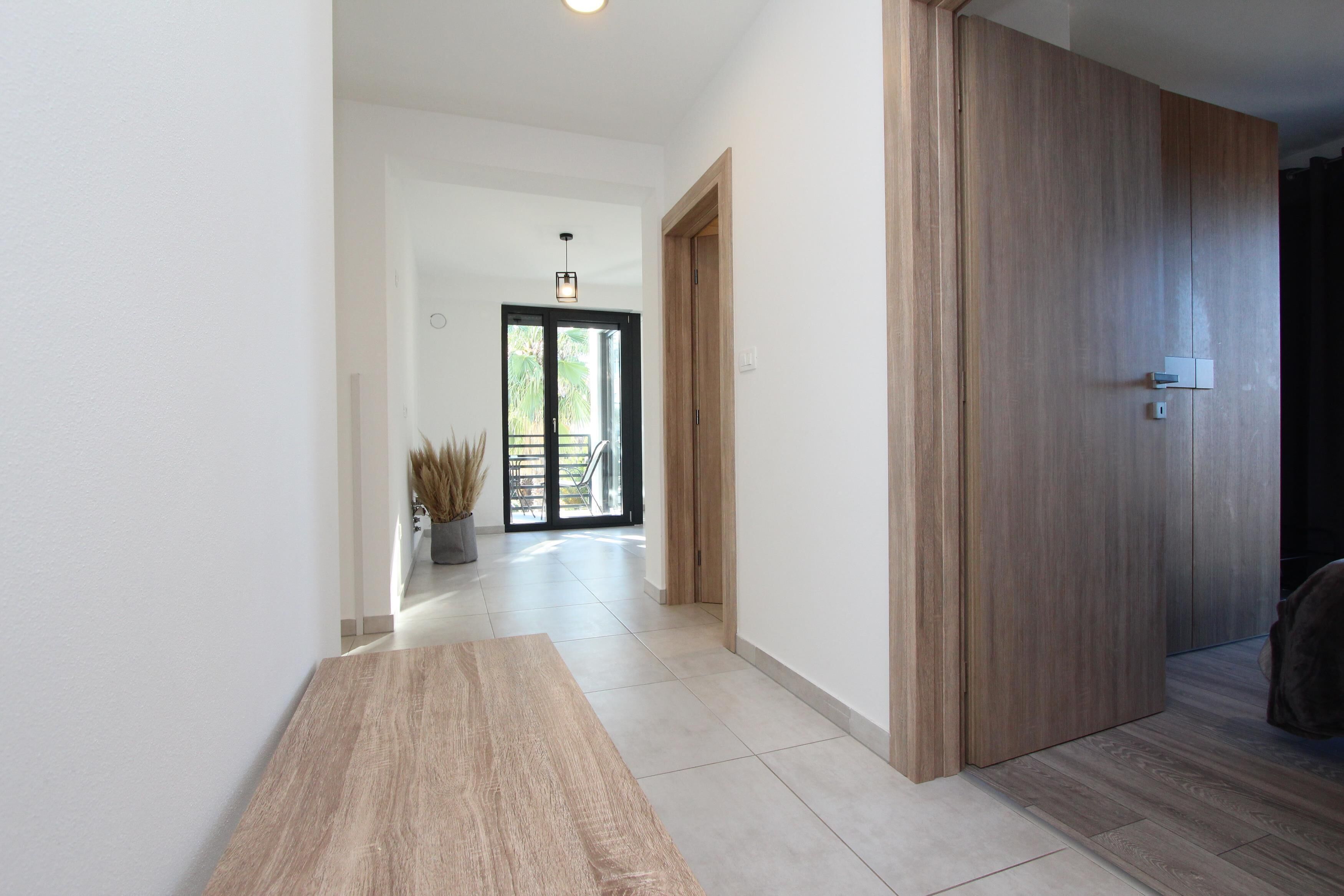 Un pasillo con un banco de madera, una planta en maceta y una puerta que da a un balcón.