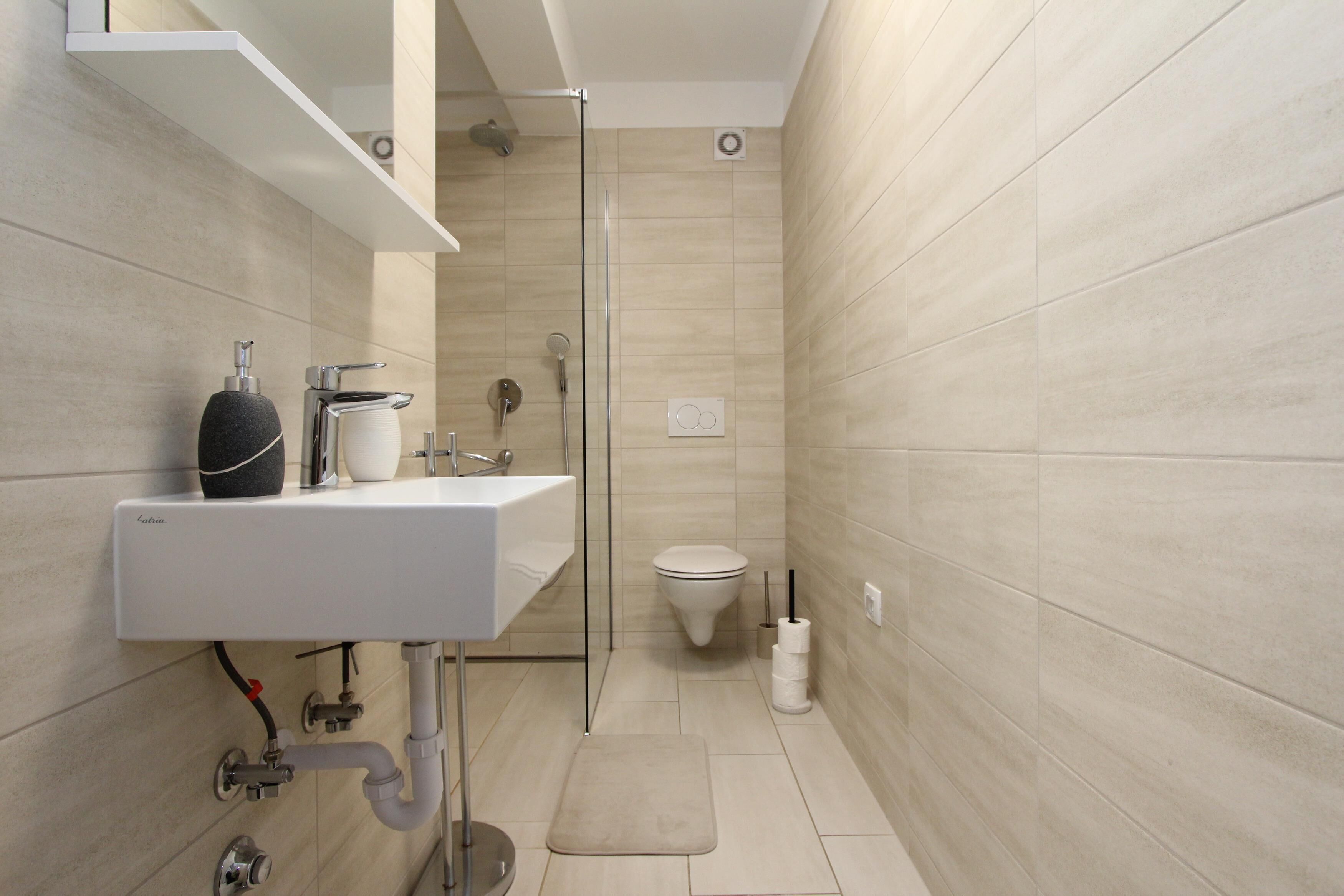 A modern bathroom with a white sink, a glass shower enclosure, and a toilet.