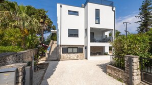 A modern two-story building with a white facade, a balcony on the upper floor, and a gravel driveway leading to a gated entrance. - Apartments Katarina (Rovinj)