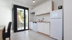 A modern kitchen with white cabinets, a dishwasher, and a refrigerator. There is a dining table with chairs and a sliding glass door leading to a balcony with outdoor furniture. - Apartments Katarina (Rovinj)