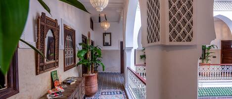 Um corredor com azulejos estampados, lanternas penduradas e um vaso de planta.