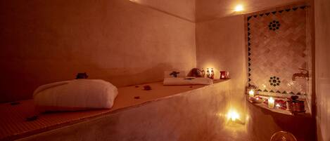Un cuarto de spa con una camilla de masaje, velas y una pequeña silla de madera.