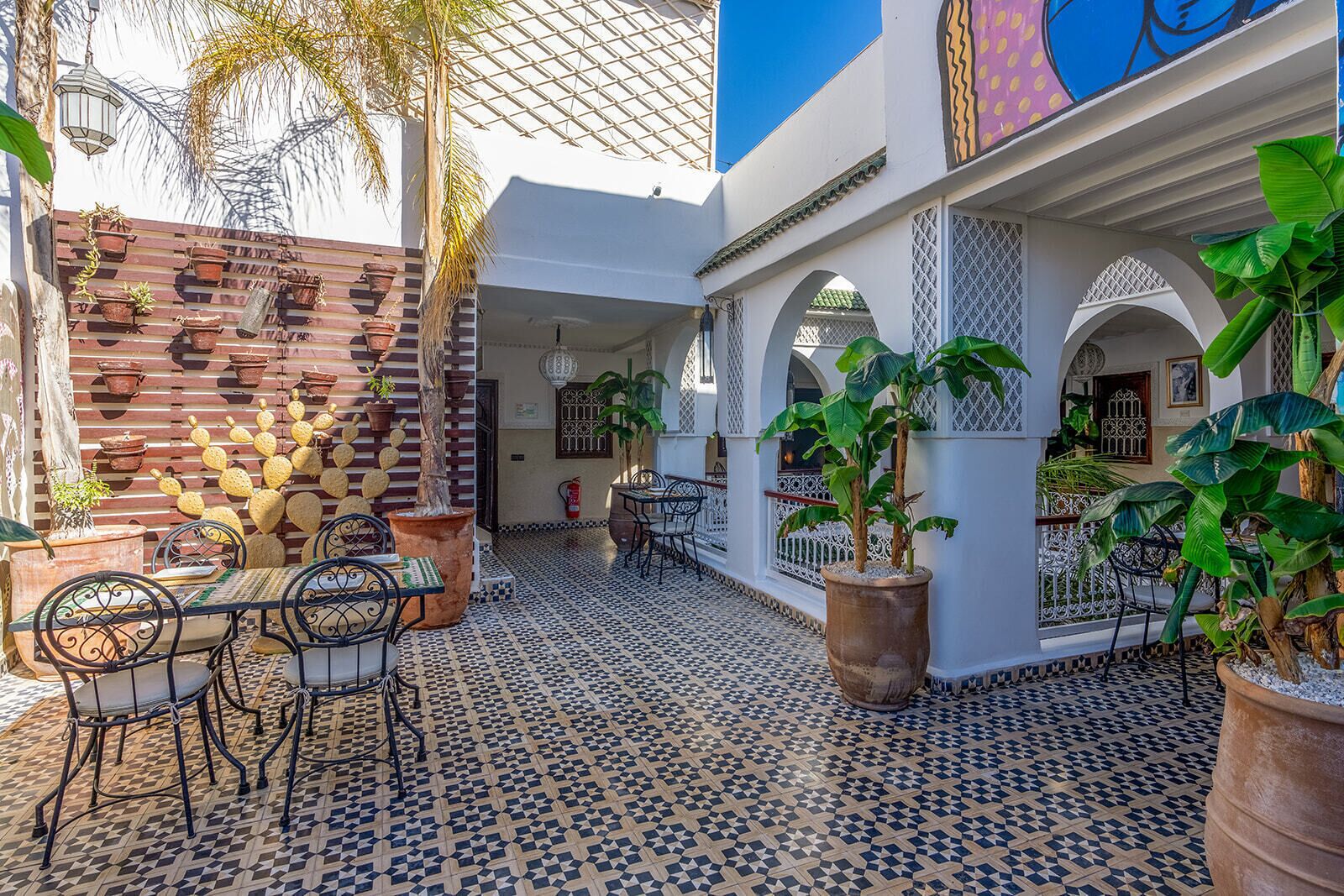 A courtyard with tiled flooring, potted plants, outdoor seating, and a decorative wall.