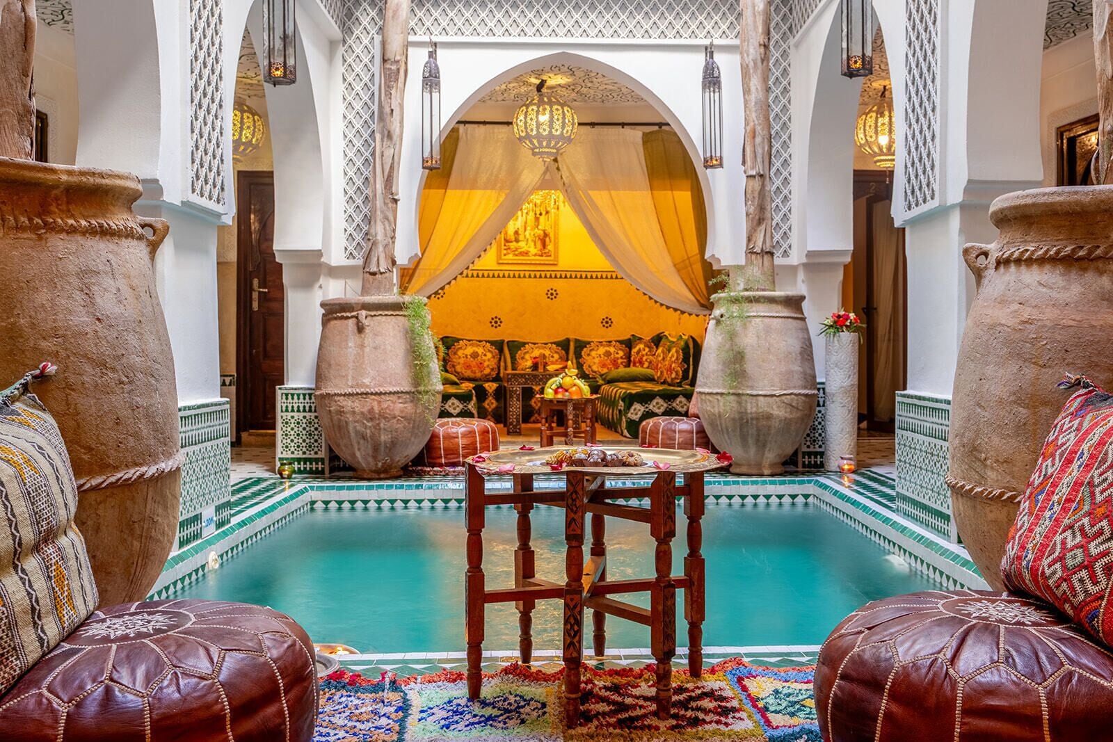 A traditional Moroccan interior with a pool, ornate furniture, and large vases.