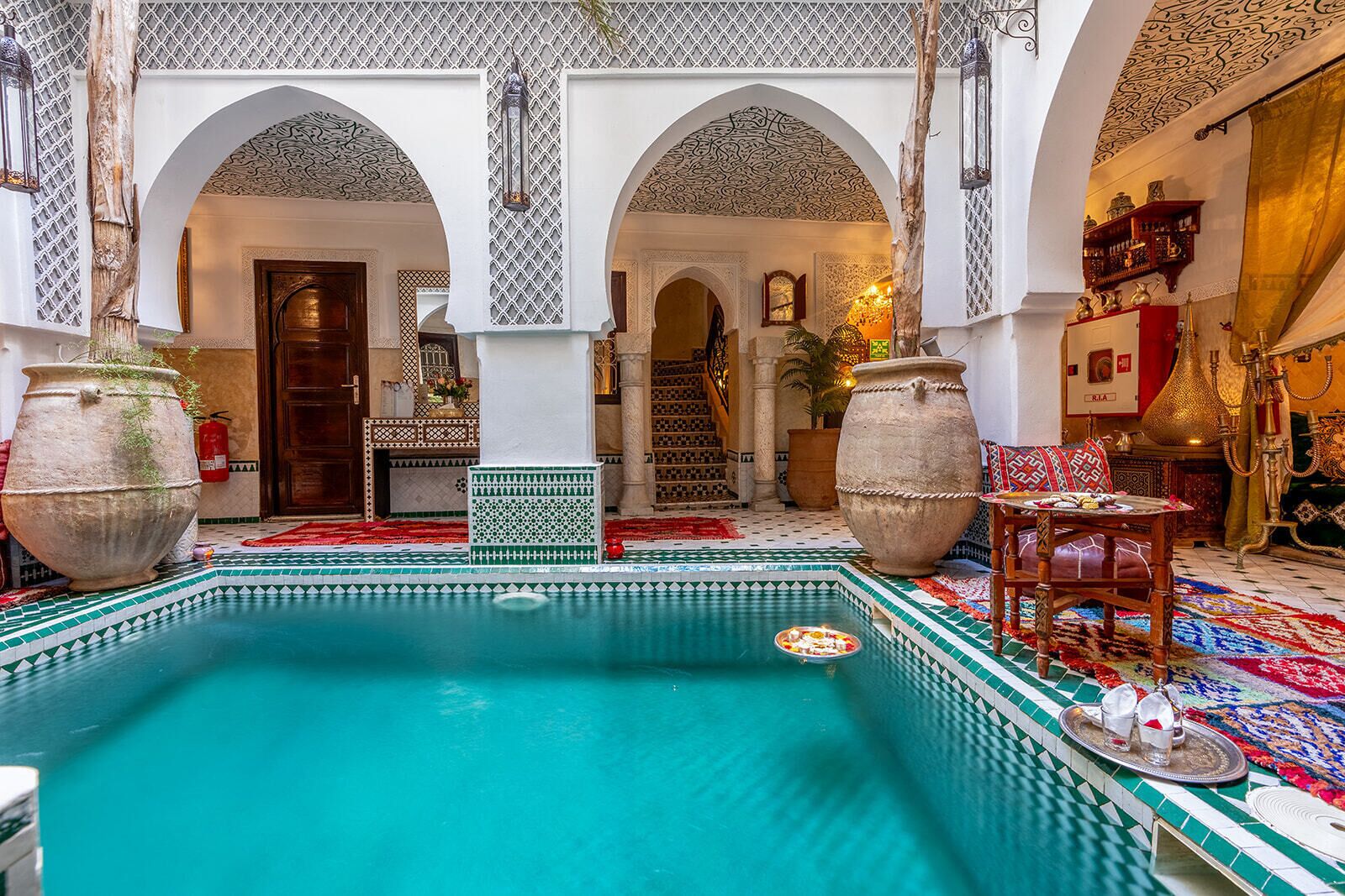 An indoor swimming pool with a tiled floor, surrounded by arches and a staircase.