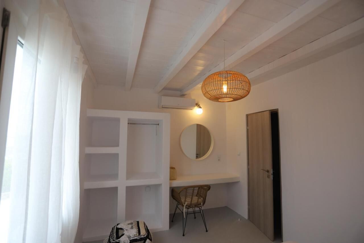 Una habitación con techo blanco, lámpara colgante, espejo, puerta de madera y una silla.