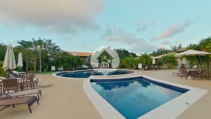 A swimming pool area with multiple pools, lounge chairs, and umbrellas. - Paraíso na Reserva Imbassaí (Mata de São João)