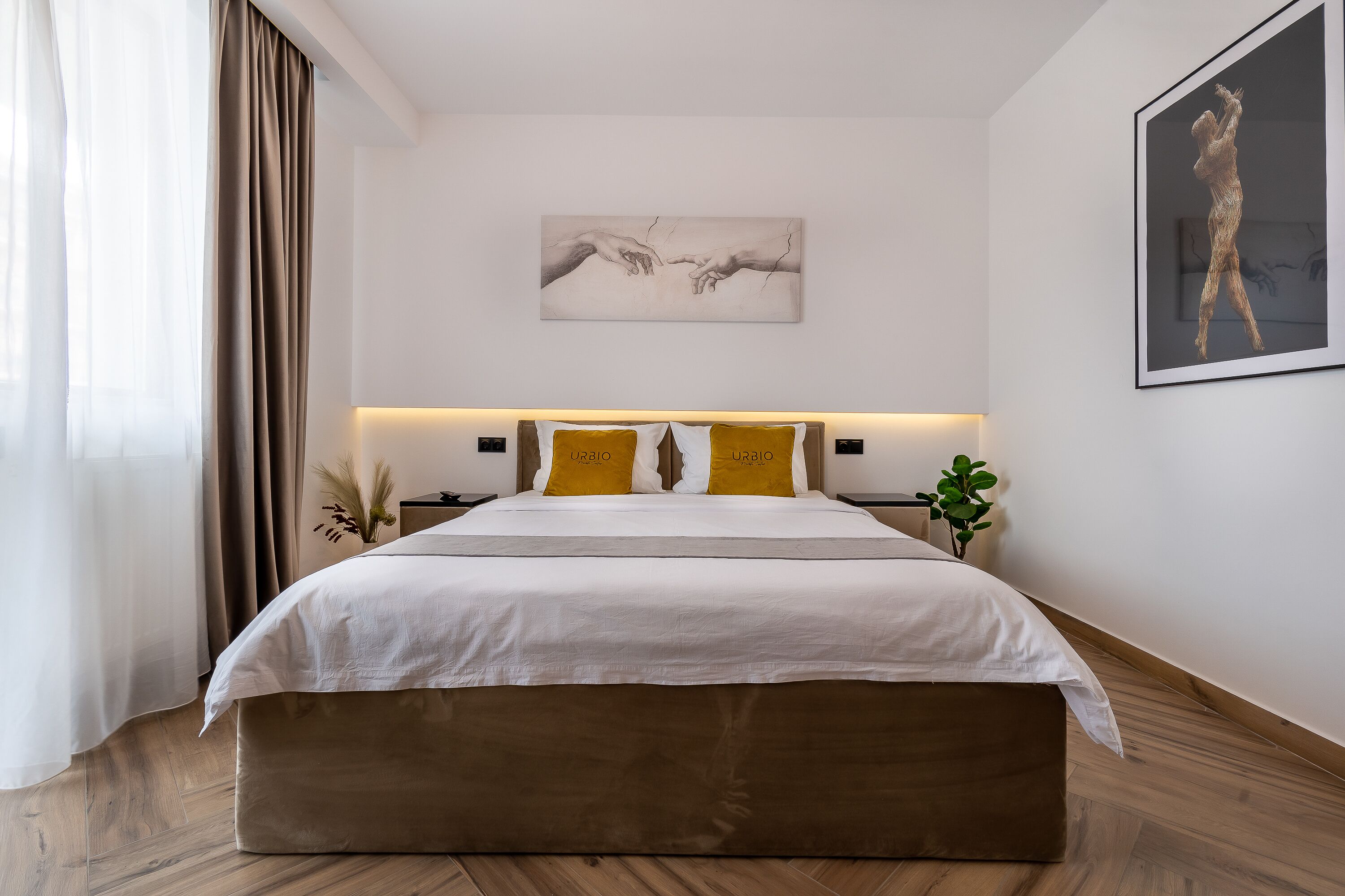 A modern bedroom with a large bed, two bedside tables, a wall-mounted artwork, and a potted plant.