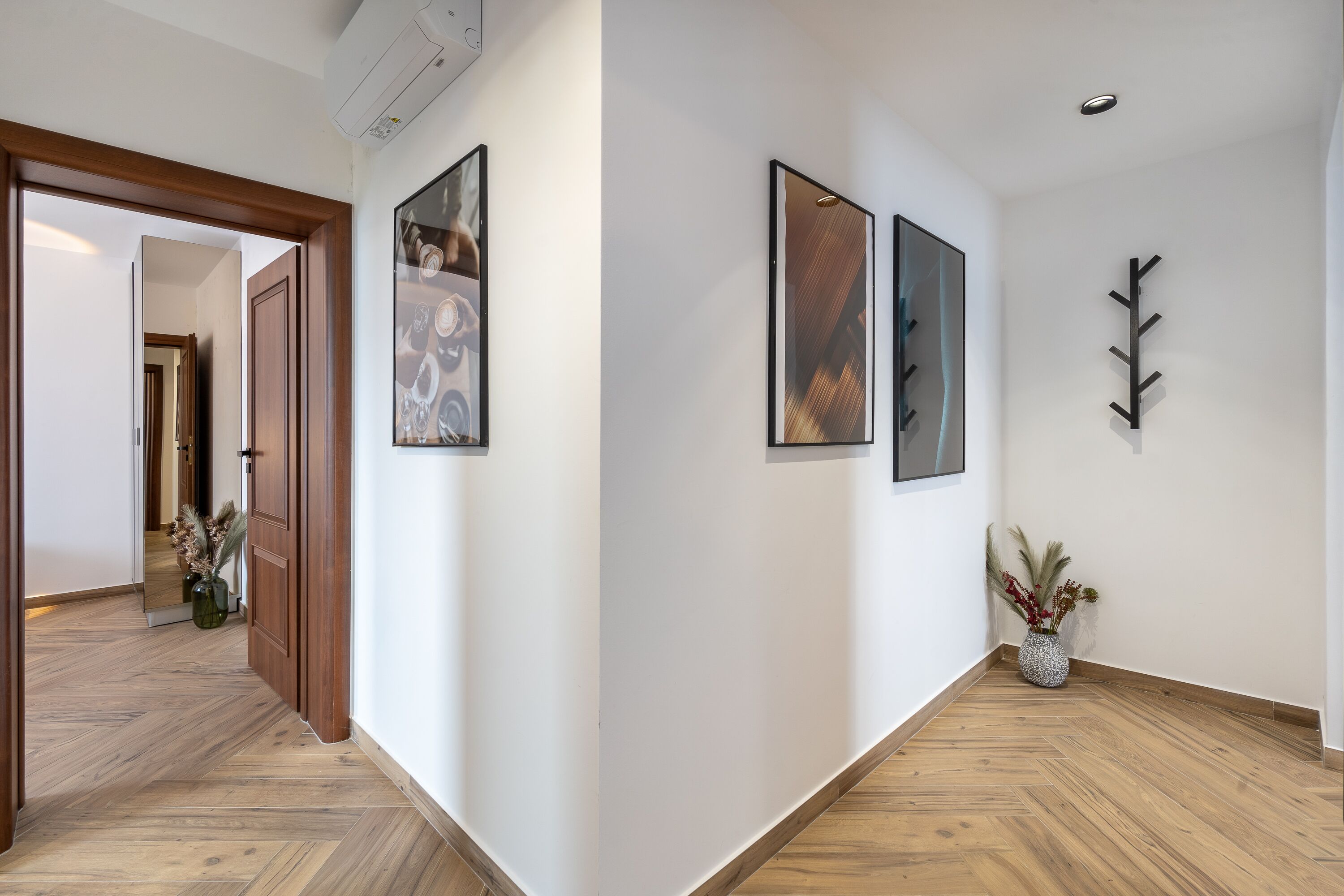 A hallway with wooden flooring, framed artwork on the walls, and a potted plant.