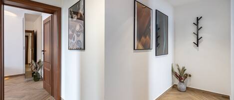 A hallway with wooden flooring, framed artwork on the walls, and a potted plant.