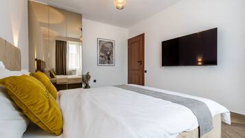 Een moderne hotelkamer met een groot bed, een flatscreen-televisie aan de muur, een houten deur en een spiegel die de kamer weerspiegelt.