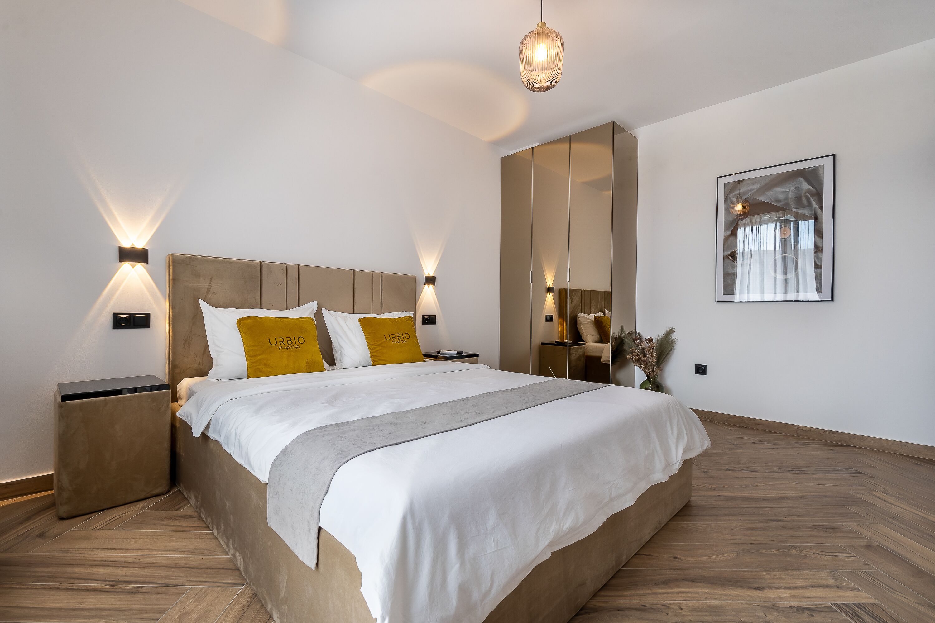 A modern bedroom with a large bed, bedside tables, a mirror, and a framed picture on the wall.