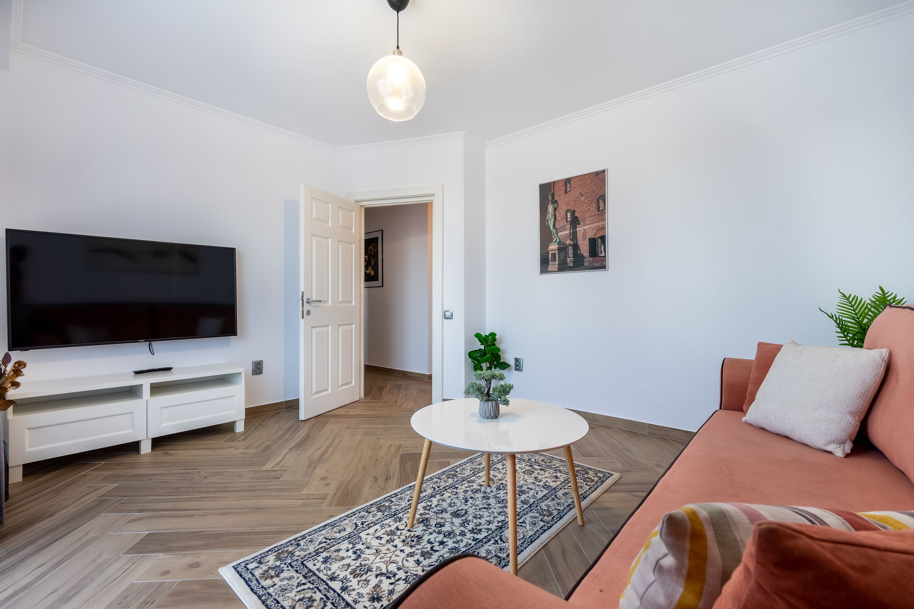A modern living room with a flat-screen TV, white entertainment unit, round coffee table, and a sofa with cushions.
