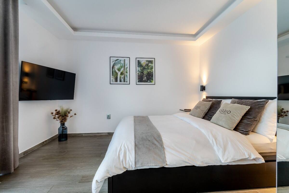 A modern bedroom with a large bed, a flat-screen TV mounted on the wall, and two framed pictures above the bed.